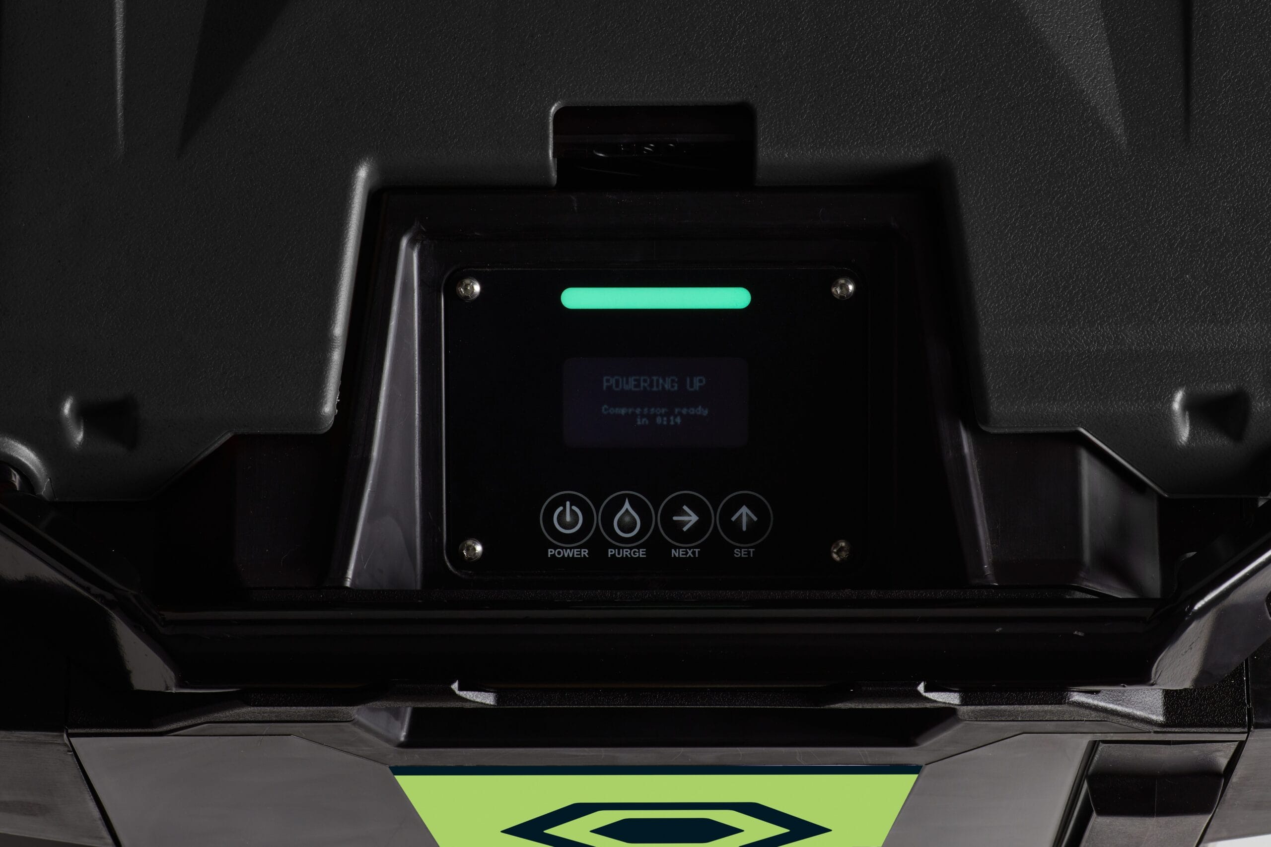 A close-up shot of a digital control panel with a glowing green light and four buttons reading: "Power", "Purge", "Next", "Set". The screen reads "Powering up... compressor is ready in 00:14".