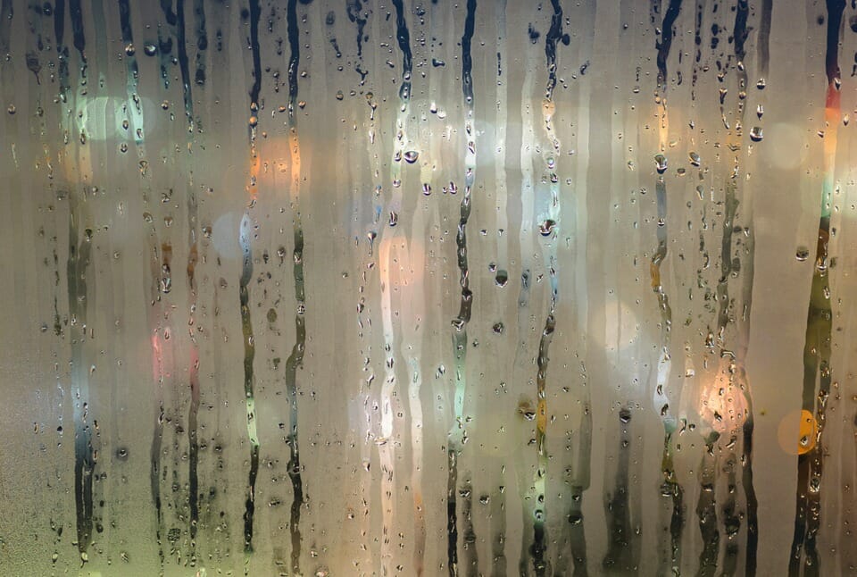 water droplets dripping down a window with lights behind it