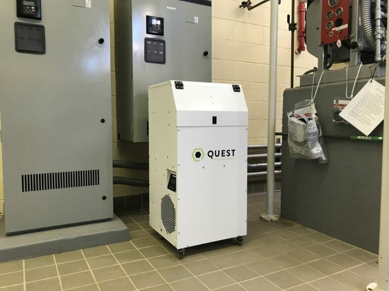 View of Quest Hi-E Dry portable dehumidifier on caster wheels. It's standing vertical on tiled floor in a water treatment facility in the background.