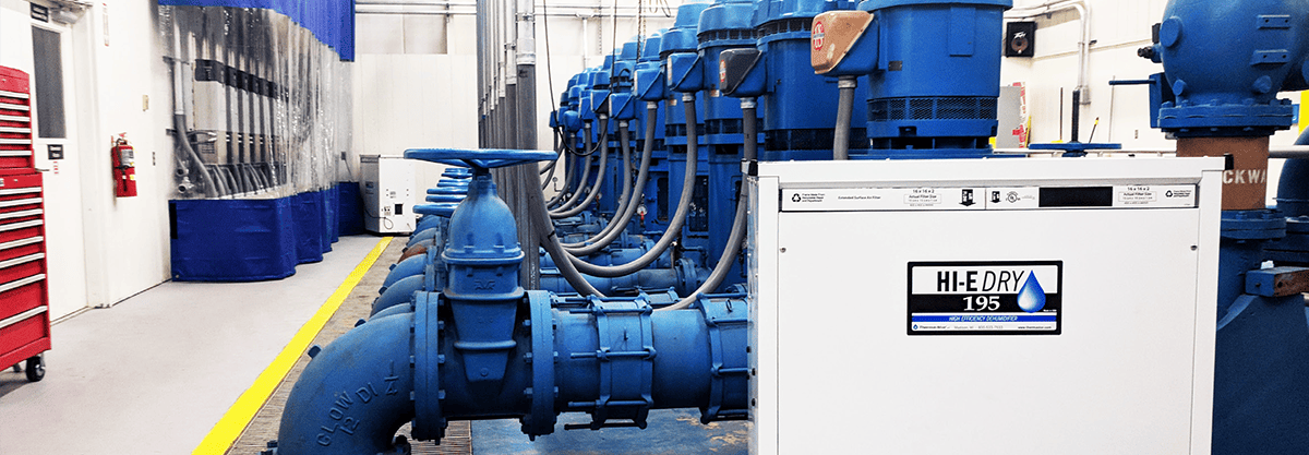 Large blue pipes in a water treatment plant with a portable Hi-E Dry 195 dehumidifier standing next to them.